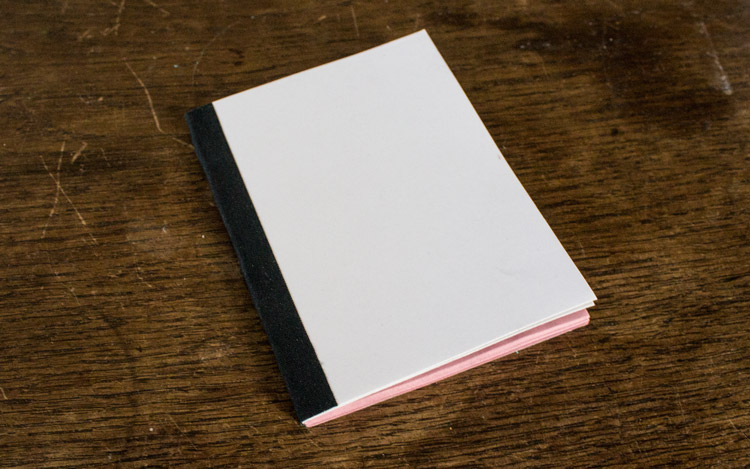 a softcover notebook with white cover and pink paper on the inside