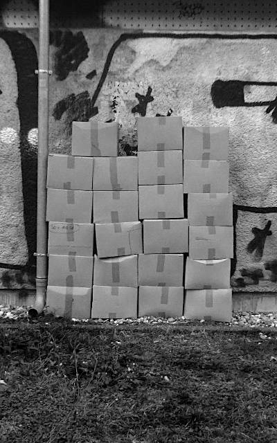 black and white photograph of stacked boxes leaning against the wall of a power house, waiting for delivery