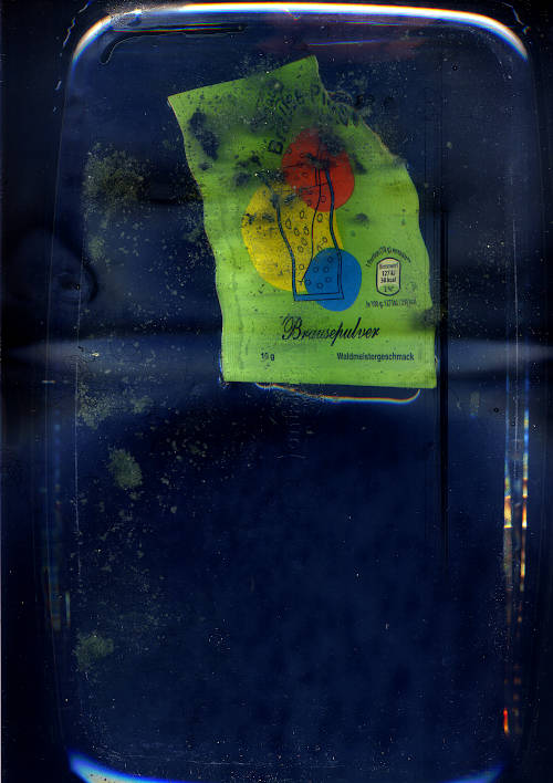 Brausepulver Waldmeistergeschmack scan image. a light green opened package of fizzy powder swimming in the water. the old clumped green content does not distribute properly in the water